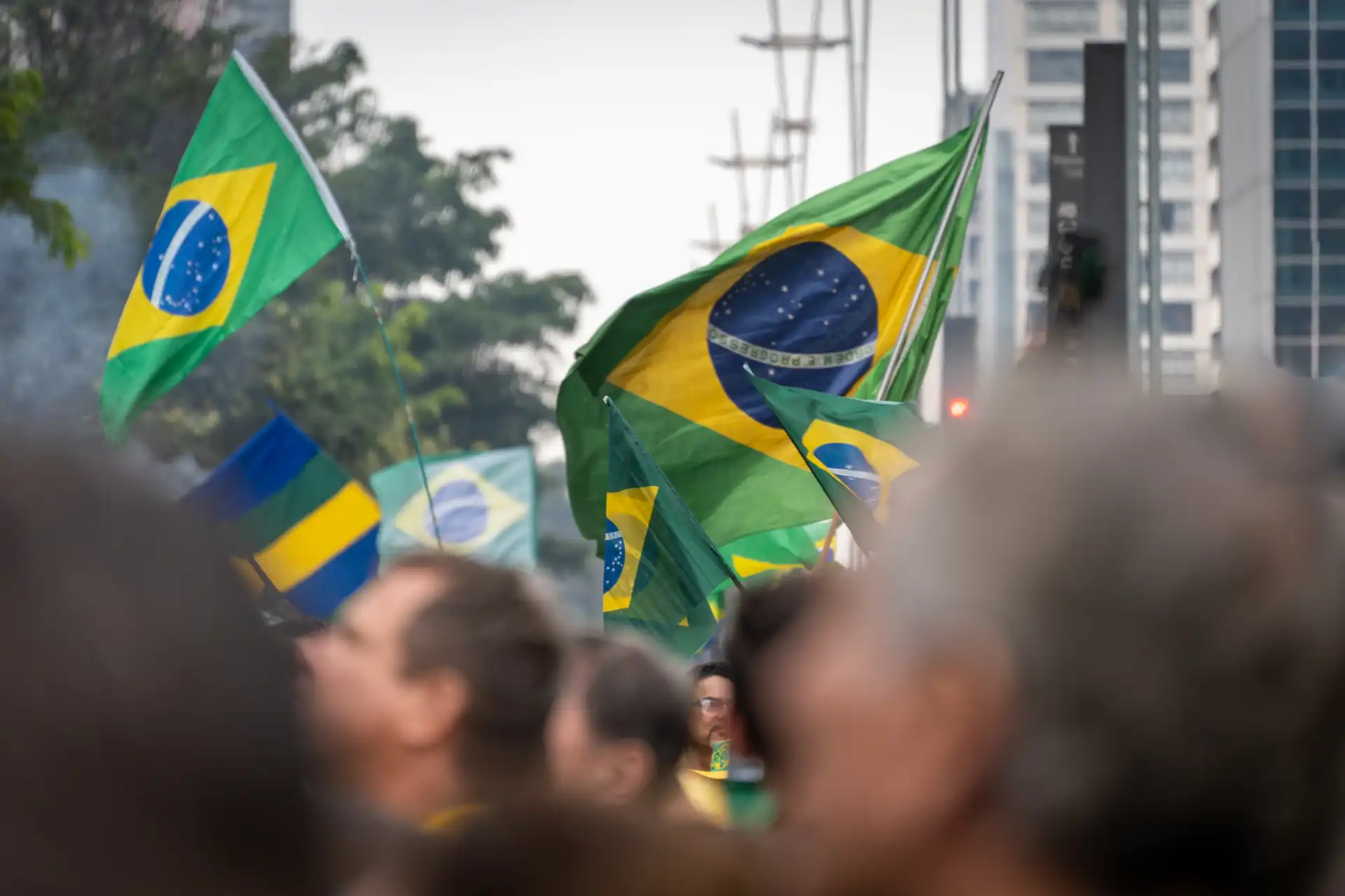 A imagem mostra uma multidão segurando bandeiras do Brasil em uma manifestação. As bandeiras verde e amarela são icônicas e simbolizam o patriotismo brasileiro. A cena retrata um momento de união entre os cidadãos, destacando a importância das manifestações cívicas no Brasil.