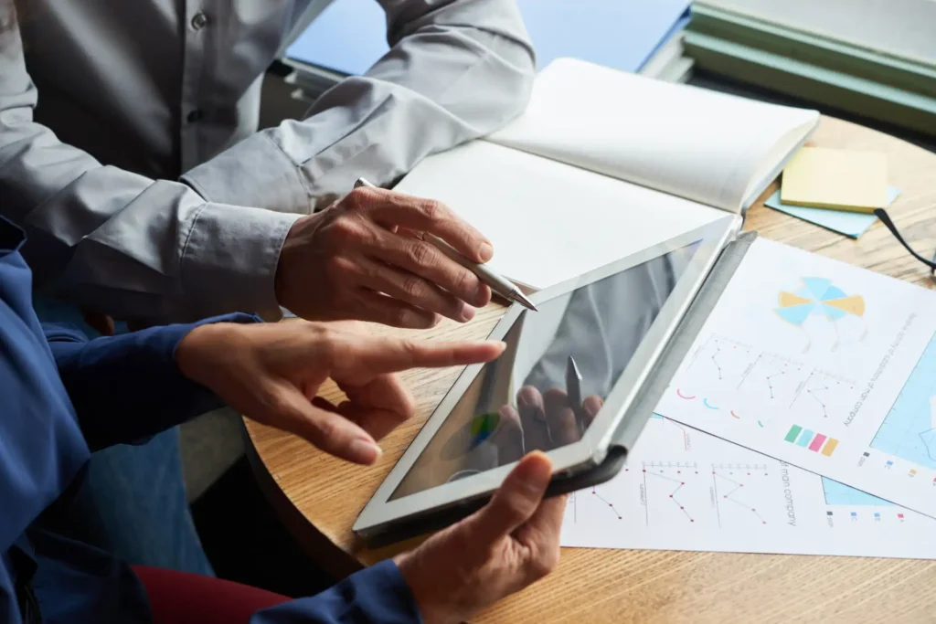 Duas pessoas analisando gráficos em um tablet enquanto discutem estratégias de negócios em um ambiente de trabalho colaborativo.