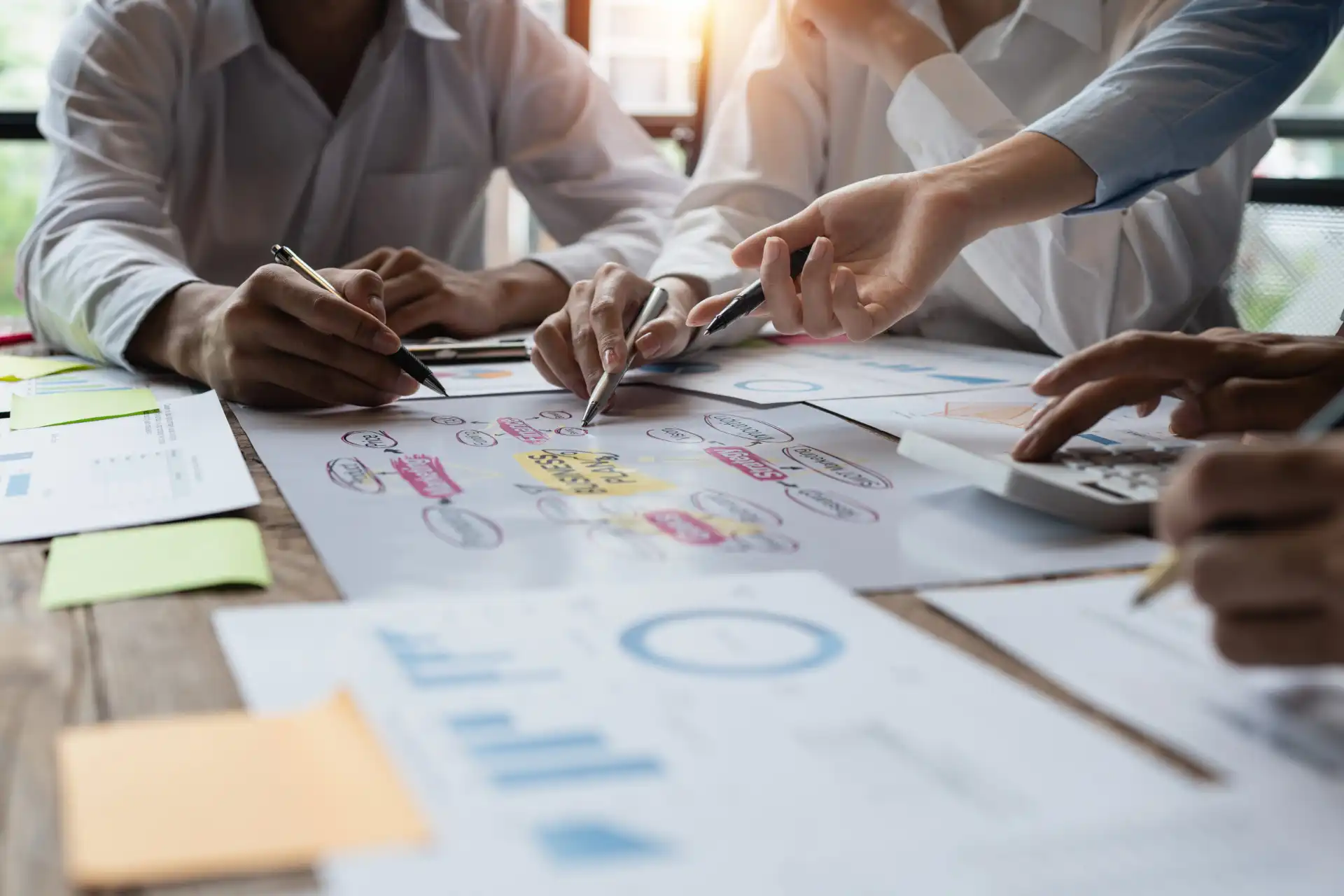 Imagem de pessoas colaborando em uma reunião, analisando gráficos e organizando ideias em um quadro branco, demonstrando trabalho em equipe e criatividade em projetos.