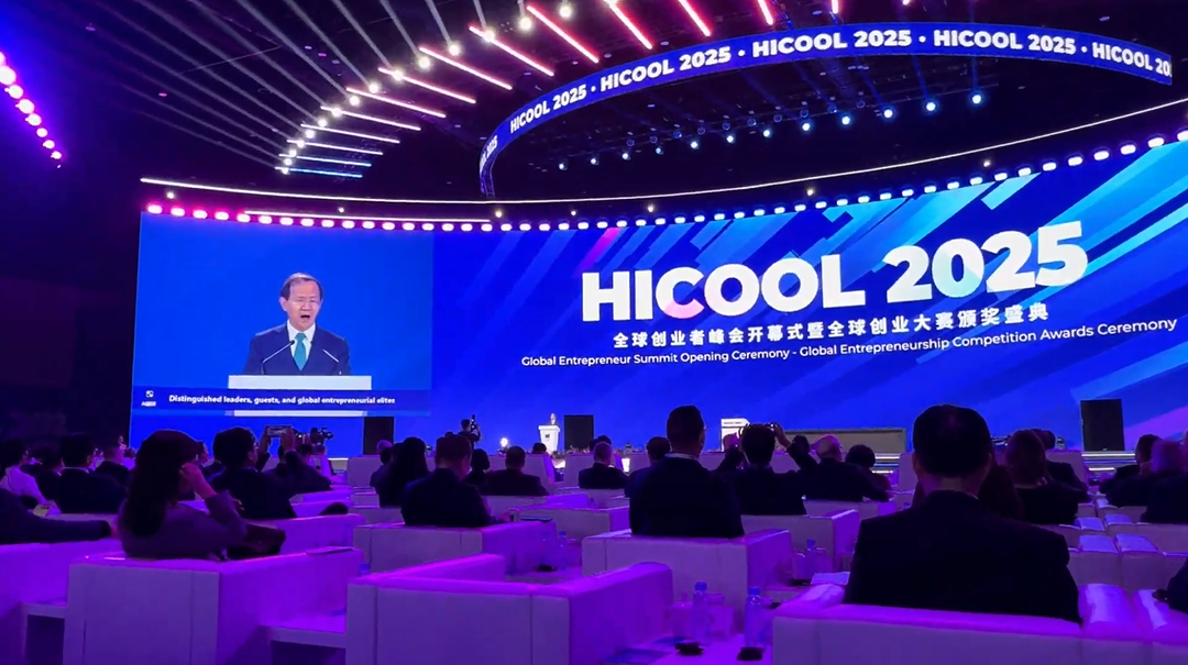 Conferência ou evento com amplo palco e tela gigante com o tema 'HICOOL 2025', iluminação colorida e público assistindo ao palestrante.